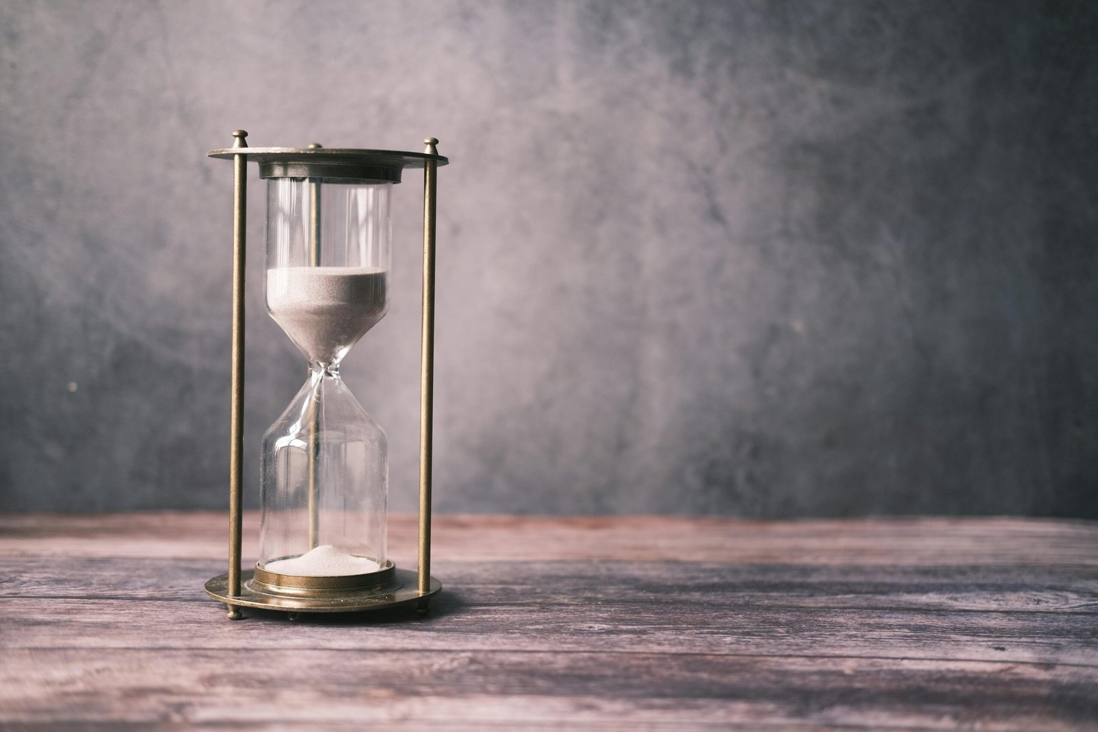 A classic hourglass with sand on a rustic wooden table against a soft gray background, offering ample copy space.